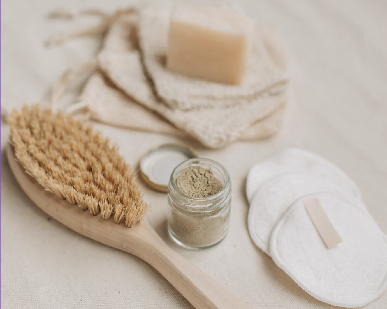 Dry brush, clay mask jar, natural soap and reusable cotton pads on soft linen
